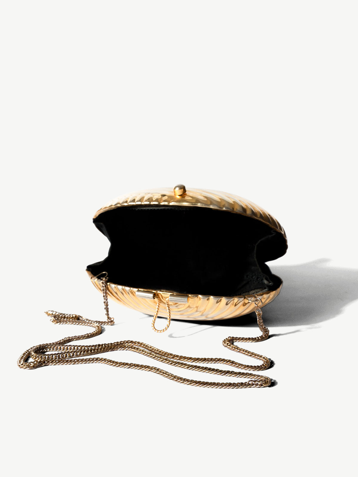 A gold-toned woven clutch bag with a black velvet interior, shown open on a clean white background with its chain strap draped in front.